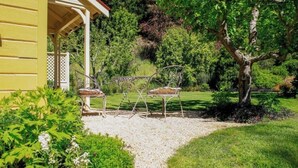 Een tuin met een prieel, twee metalen stoelen en een grindpad.