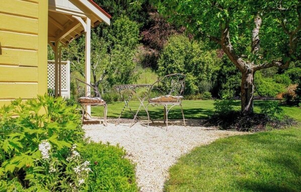 A garden with a gazebo, two metal chairs, and a gravel path.
