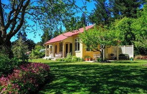 A yellow house with a red roof, surrounded by lush greenery and a well-maintained lawn.