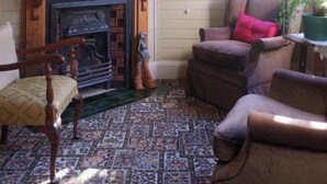 Een gezellige kamer met een open haard, een raam met uitzicht op groen, en een kamer met een patroon vloer.
