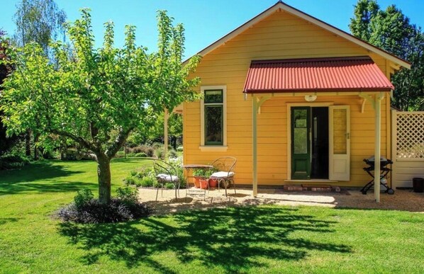 A yellow wooden house with a red roof, a small porch, and a tree in the front yard.