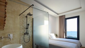 A modern hotel room with a glass-enclosed shower, a large bathtub, two beds with a view of the sea, and a wooden floor. - Two bedroom villas with private pool (Kalamitsa)