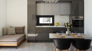 A modern kitchen with dark cabinets, a built-in oven, and a dining area with a table set for two. - Two bedroom villas with private pool (Kalamitsa)