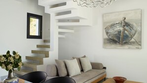 A modern living room with a sofa, dining table, and staircase. - Two bedroom villas with private pool (Kalamitsa)