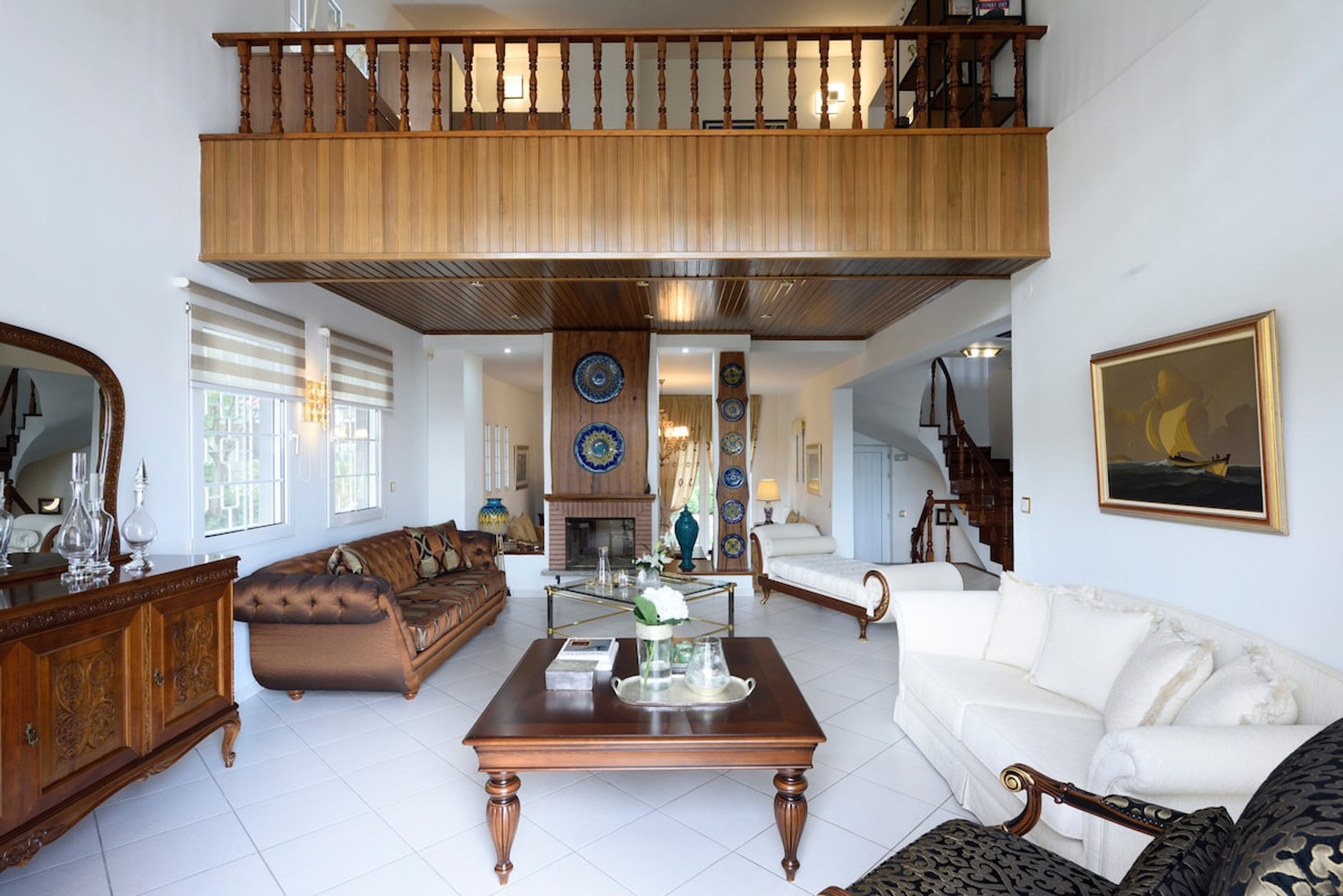 A spacious living room with a high ceiling, a wooden staircase, and a view of the upper floor.