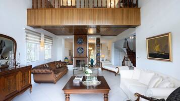 A spacious living room with a high ceiling, a wooden staircase, and a view of the upper floor.