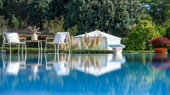 A serene outdoor pool area with lounge chairs and a table, surrounded by lush greenery and a white tent-like structure.