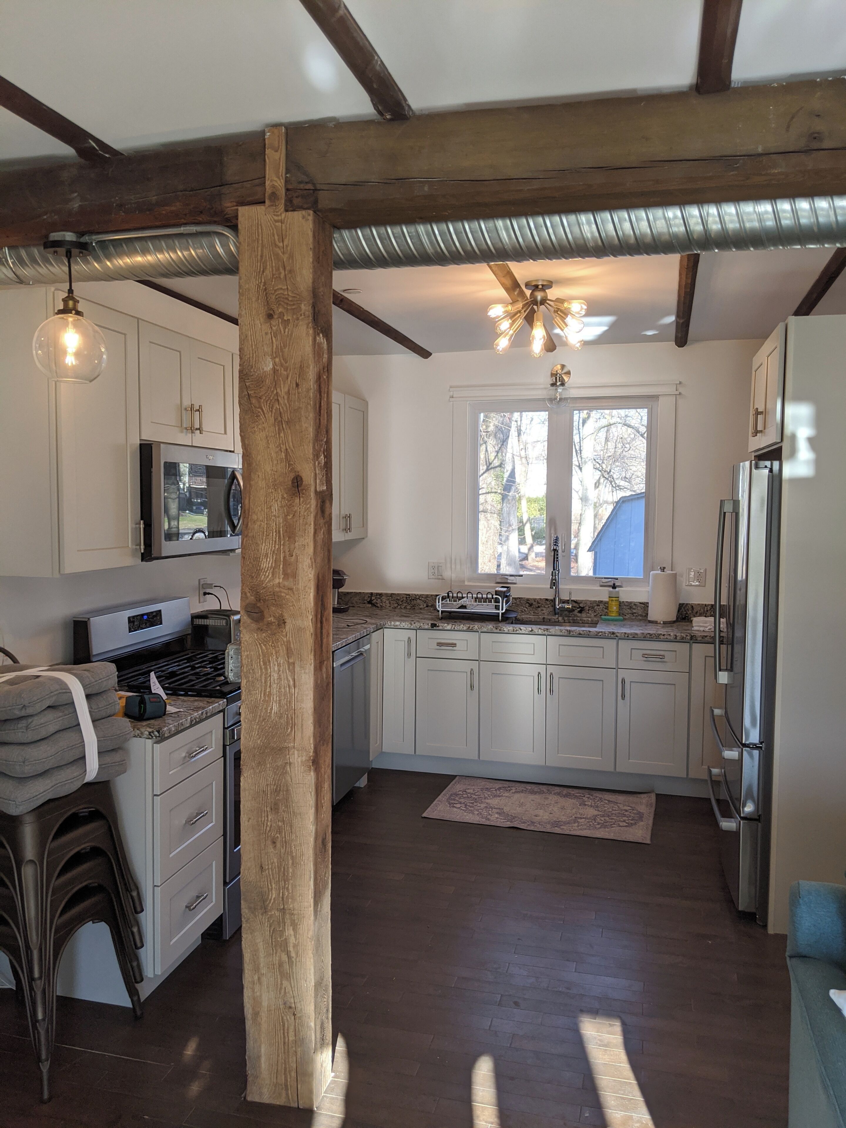 A kitchen with white cabinets, a stainless steel refrigerator, a microwave, a stove, and a wooden beam structure.