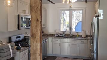 A kitchen with white cabinets, a stainless steel refrigerator, a microwave, a stove, and a wooden beam structure.