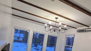 A bedroom with a bed, a chandelier, large windows, and a ceiling vent.