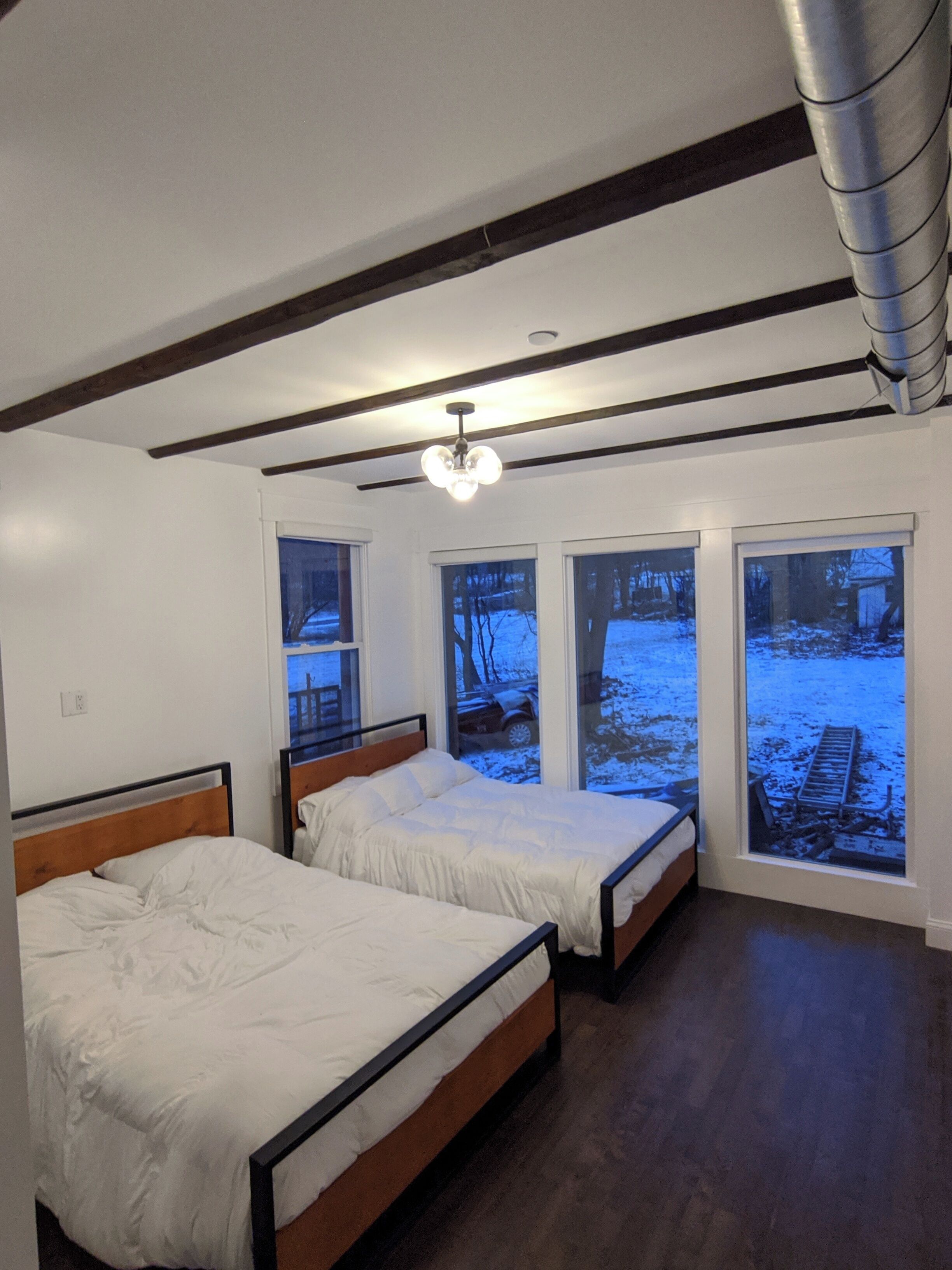 Un dormitorio con dos camas, ventanas amplias y una viga de techo de madera.