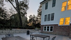 An outdoor patio with a wooden table and metal chairs, a hammock, and a brick wall. - Historic Horse Barn Apartment in Goshen (Goshen)