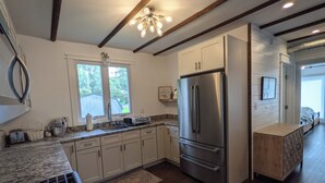 A modern kitchen with stainless steel appliances, wooden beams, and a large window. - Historic Horse Barn Apartment in Goshen (Goshen)