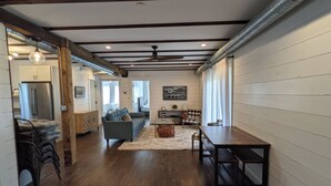 A spacious living area with a wooden floor, a sofa, a dining table, and a ceiling fan. - Historic Horse Barn Apartment in Goshen (Goshen)