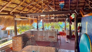 Un área de comedor al aire libre con techo de paja, chimenea de ladrillo y vista al océano.