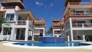 Un resort con edificios de dos pisos, una piscina central y construcciones con techo de paja.