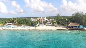 Un hotel frente a la playa con varias edificaciones, una playa de arena y agua turquesa cristalina.