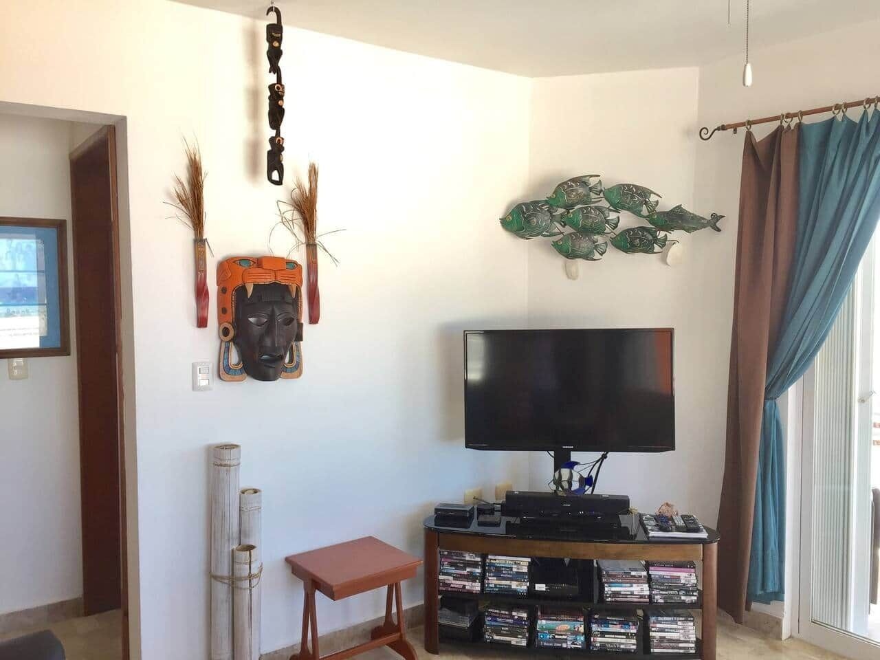 A living room with a flat-screen TV, a small wooden table, and a wall-mounted shelf with DVDs.