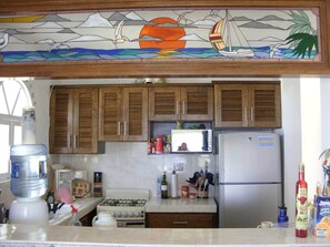 A kitchen with wooden cabinets, a microwave, a refrigerator, and various kitchen items on the counter.