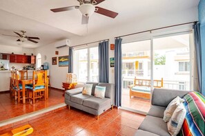 Un vaste espace de vie comprenant un canapé, une table à manger avec des chaises, un ventilateur de plafond et une vue sur l’extérieur.