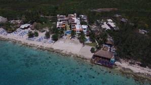 Luftaufnahme eines Resorts mit mehreren Gebäuden, einem Strand und klarem, türkisblauem Wasser.