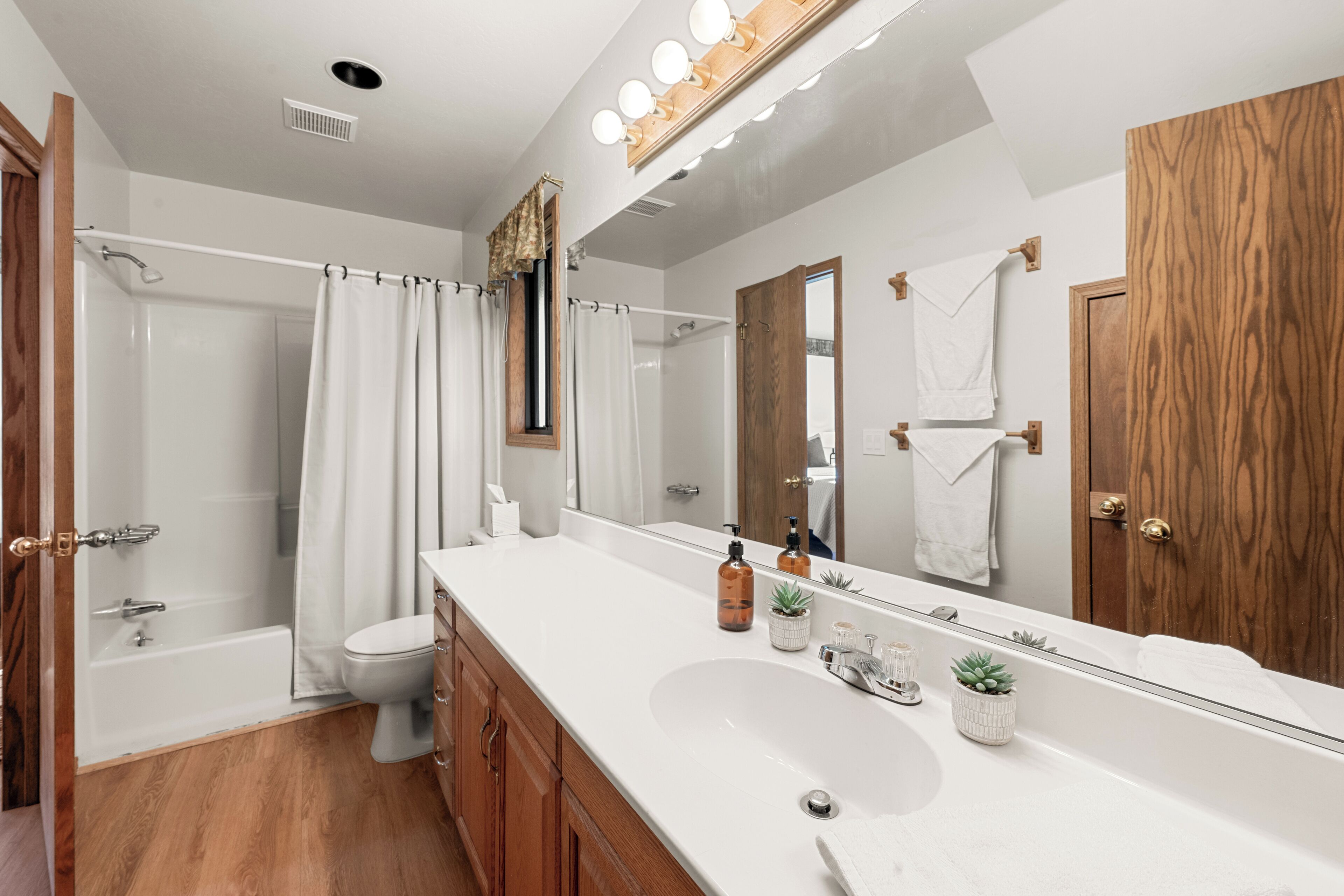 A modern bathroom with a large mirror, a bathtub, a shower, and a sink.