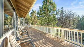 A wooden deck with chairs, a railing, and a view of trees. - Beau Bear (Big Bear City)