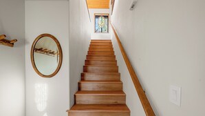 A wooden staircase with a handrail, a circular mirror on the wall, and a window at the top. - Beau Bear (Big Bear City)