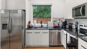 Una cocina moderna con electrodomésticos de acero inoxidable, lavavajillas y ventana con vista a árboles.