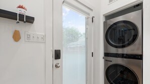 Un cuarto de lavandería con dos lavadoras de carga frontal, una puerta con panel de vidrio esmerilado, un interruptor de luz y un pequeño objeto decorativo en la pared.
