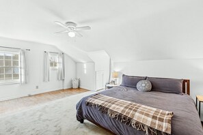 Une chambre spacieuse avec un grand lit, un ventilateur de plafond et une fenêtre avec des rideaux.