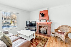 Un salon avec une cheminée, un téléviseur, une table basse blanche et un fauteuil en osier.