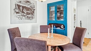 Een eetruimte met een ronde houten tafel, vier stoelen, een hanglamp en een blauwe kast met glazen deuren.