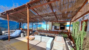 An outdoor patio with stone seating, a barbecue area, and a thatched roof structure. - Hostal Amigo Lucho  (San Pedro de Atacama)