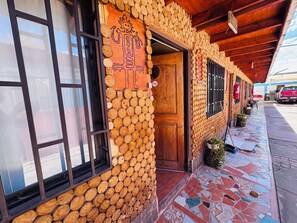 Un bâtiment dont la façade extérieure est recouverte de bois et ornée de rondins de bois empilés, avec une porte en bois et un hall d’entrée carrelé.