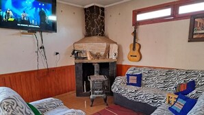 A living room with a television, a fireplace, a guitar, and a patterned sofa. - Hostal Amigo Lucho  (San Pedro de Atacama)