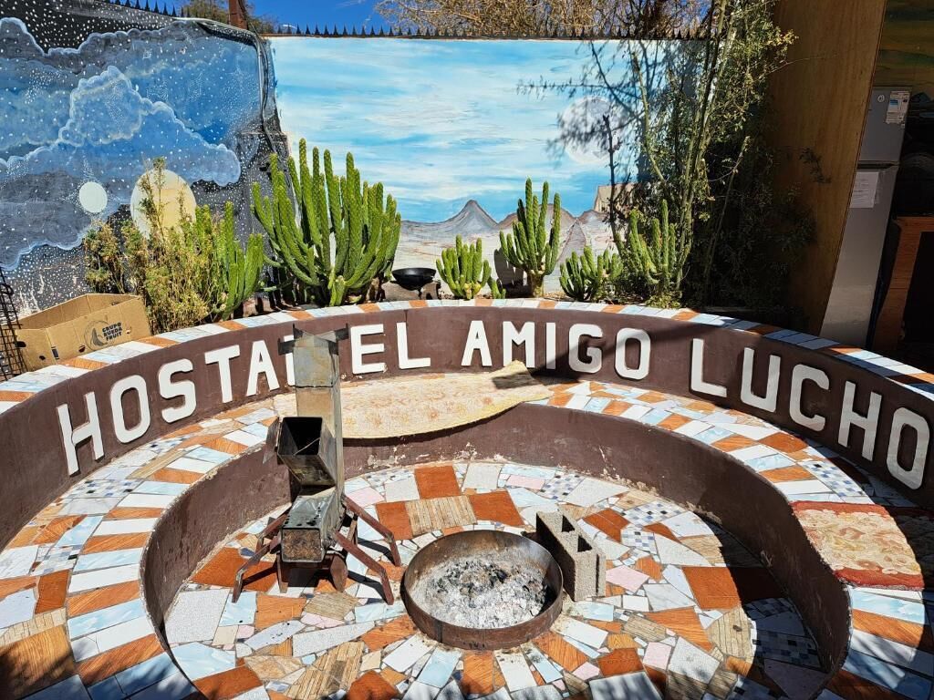 Uma área de estar externa circular com lareira, rodeada por um chão de mosaico e identificada como 