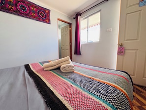 A room with a bed, a colorful blanket, a door with a sign, and a window with curtains.