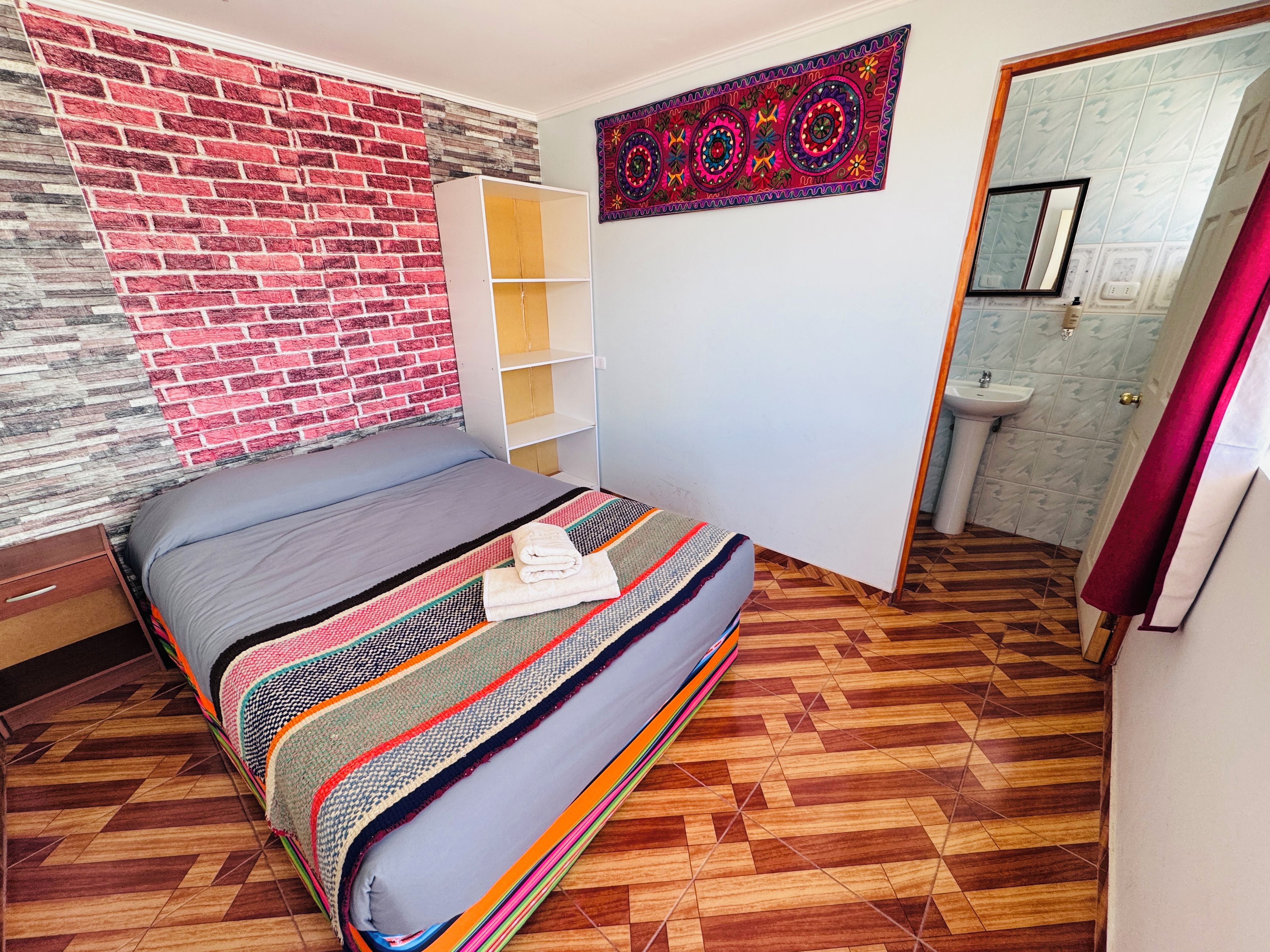 Ein Schlafzimmer mit Bett, Schrank und einem Badezimmer mit Waschbecken, sowie einer Wand mit Muster.