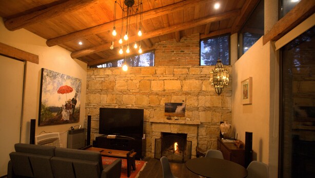 A living room with a stone fireplace, a flat-screen TV, a sofa, and a dining table with chairs. - Maceiras House (San Cristóbal de las Casas)