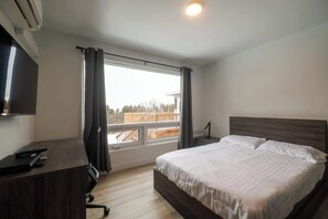 Un dormitori amb un llit, escriptori, cadira, televisió i finestra amb cortines.