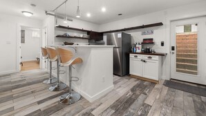 Une cuisine moderne dotée d’un îlot central, de tabourets de bar, d’un réfrigérateur et d’une porte en bois.