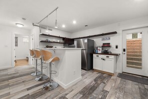 Cozinha moderna com ilha central, banquetas, geladeira de aço inoxidável e porta de madeira.