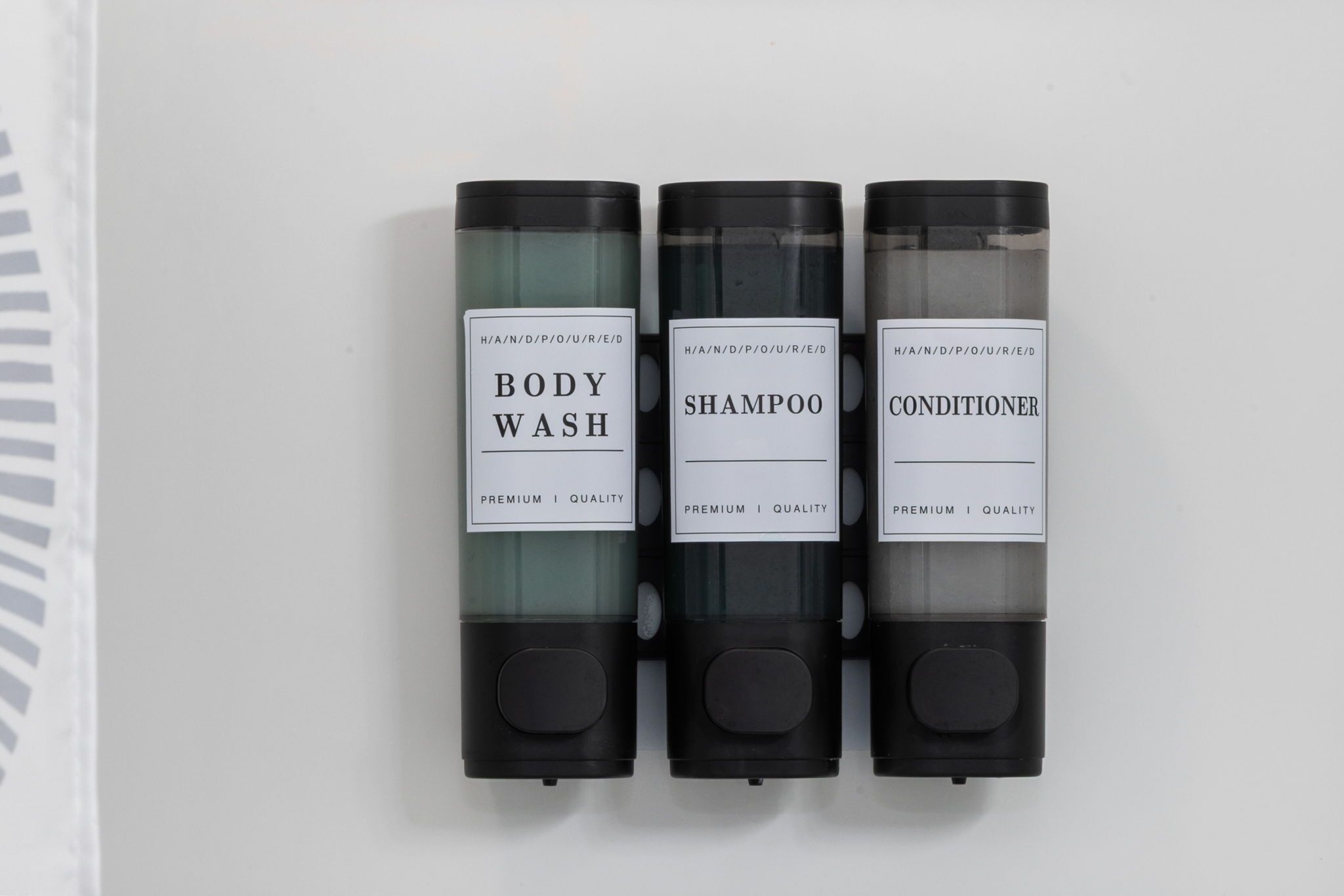 Tres botellas de gel de baño, champú y acondicionador sobre una superficie blanca.
