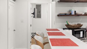 Une cuisine moderne avec des meubles blancs, une longue table à manger agrémentée de sets de table rouges et un four à micro-ondes posé sur le plan de travail.