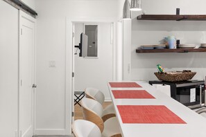 Uma cozinha moderna com armários brancos, uma mesa de jantar comprida com jogos americanos vermelhos e um micro-ondas na bancada.