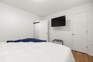 Ein Schlafzimmer mit einem Bett, einem an der Wand montierten Fernseher und einer Tür zu einem Kleiderschrank.