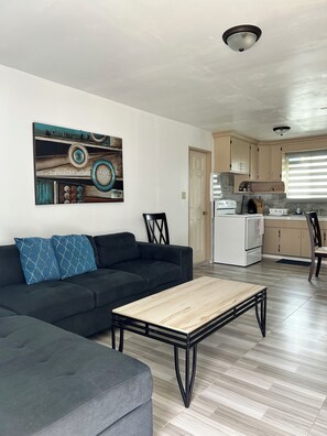 A living room with a sofa, a coffee table, and a kitchen in the background. - Cozy 2-bedroom apartment in soothing Mangilao with AC (Mangilao)