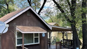 Una pequeña cabaña de madera con un porche, una antena parabólica y un letrero que dice 'Bienvenido'.