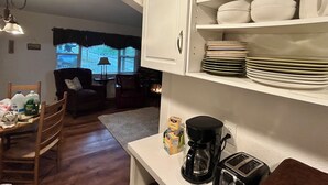 Una cocina con armarios blancos, una cafetera y un tostador. Hay un comedor con sillas y una mesa.